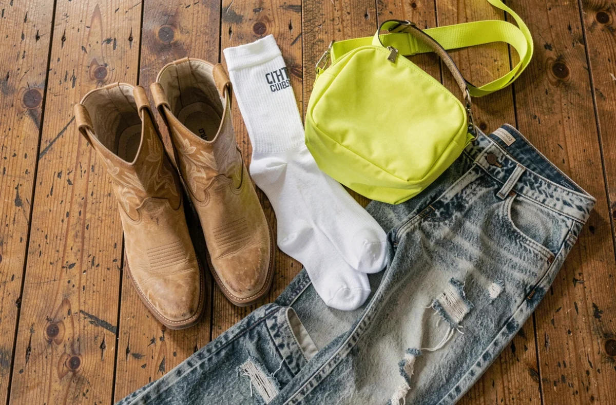 Flat lay de bottes cowboy western beiges associées à des chaussettes blanches de sport, un sac fluo et un jean délavé, illustrant les erreurs de style courantes