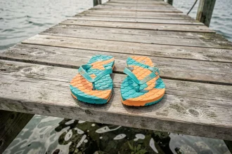 Paire de tongs en forme de poisson colorées posées sur un ponton en bois usé au bord de la mer